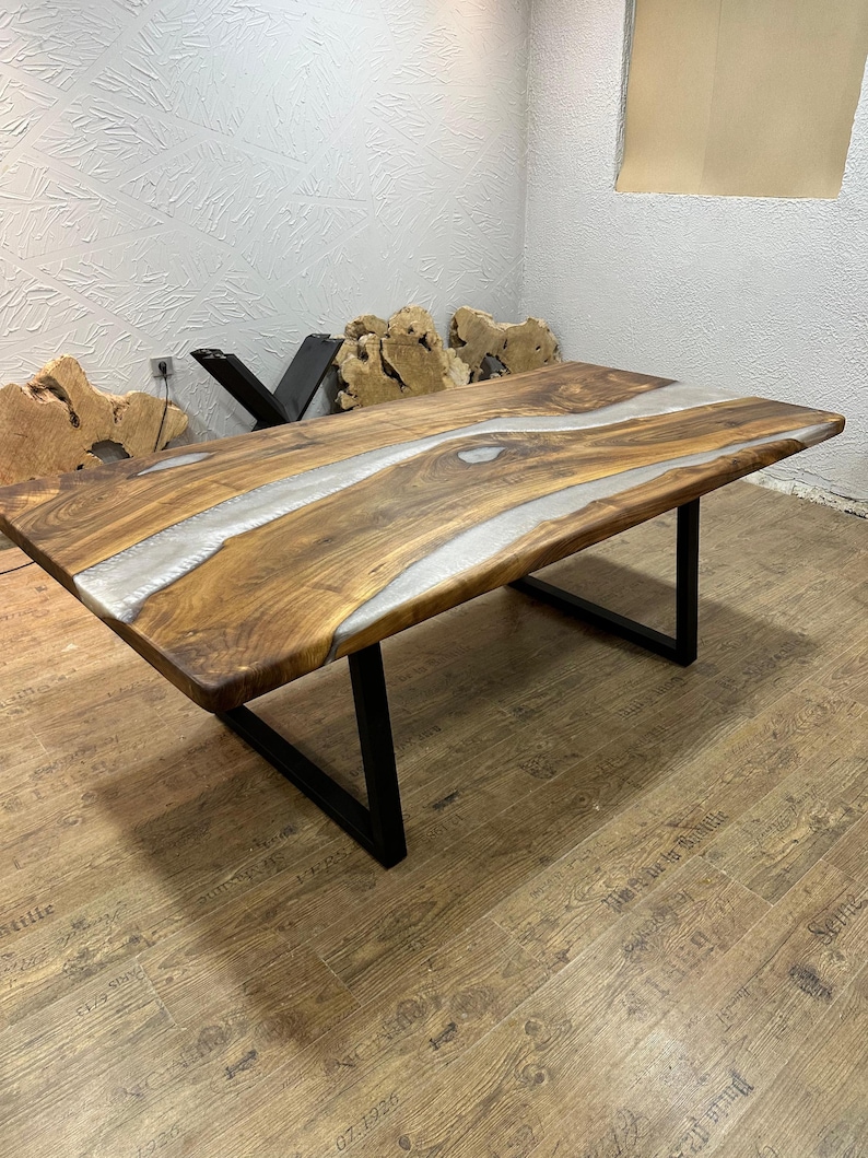 以下が含まれることがあります： ライブエッジデザインと透明なエポキシ樹脂の川がある長方形の木製テーブル。テーブルは天然の木目仕上げで、黒い金属製の脚で支えられています。テーブルの長さは約183cmです。