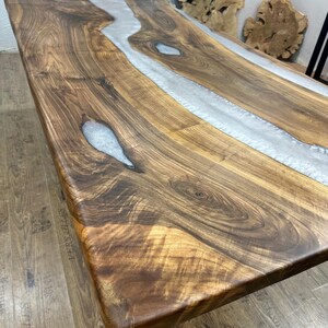 以下が含まれることがあります： 中央に銀色の樹脂の川がある長方形の木製テーブル。 テーブルは木目がはっきり見える濃い茶色の木材でできており、長さは約183cmです。