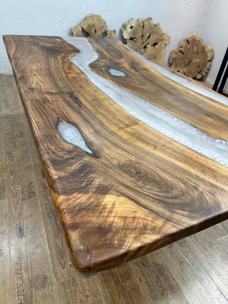 以下が含まれることがあります： 中央に銀色の樹脂の川がある長方形の木製テーブル。 テーブルは木目がはっきり見える濃い茶色の木材でできており、長さは約183cmです。