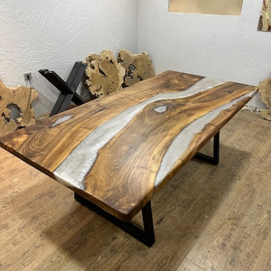 以下が含まれることがあります： 中央に銀色の樹脂の川が流れる、手作りの木製テーブル。 テーブルは濃い茶色の仕上げで、黒い金属製のベースが付いています。 テーブルの長さは約183cm、幅は約91cmです。