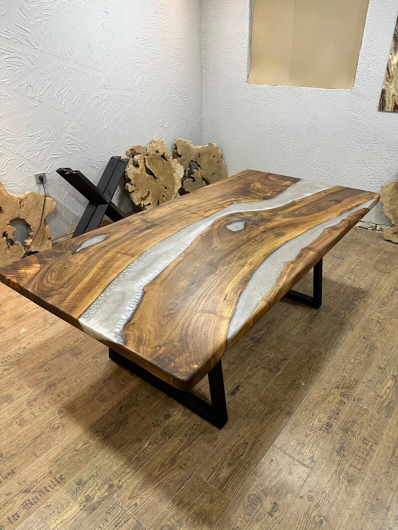 以下が含まれることがあります： 中央に銀色の樹脂の川が流れる、手作りの木製テーブル。 テーブルは濃い茶色の仕上げで、黒い金属製のベースが付いています。 テーブルの長さは約183cm、幅は約91cmです。