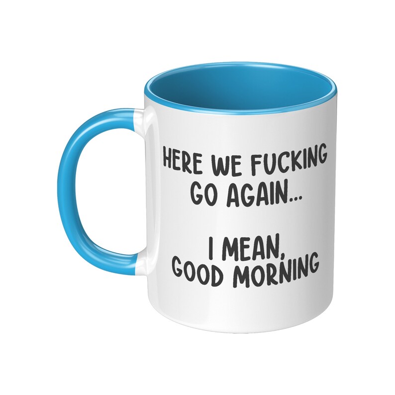 May include: White ceramic mug with a blue interior and handle. The mug features the text "HERE WE FUCKING GO AGAIN... I MEAN, GOOD MORNING" in black, bold font. The mug is designed for hot beverages.
