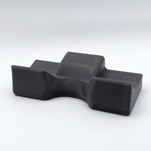 May include: A dark gray, 3D-printed object with a unique shape. It features a central raised section flanked by two lower, rectangular platforms. The object has a smooth, matte finish and appears to be made of a solid material.