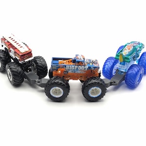 May include: Three toy monster trucks, one red and white fire truck, one orange and blue monster truck with "BIGFOOT" and "HO WHEELS" printed on the side, and one blue and green monster truck. The trucks are connected together.