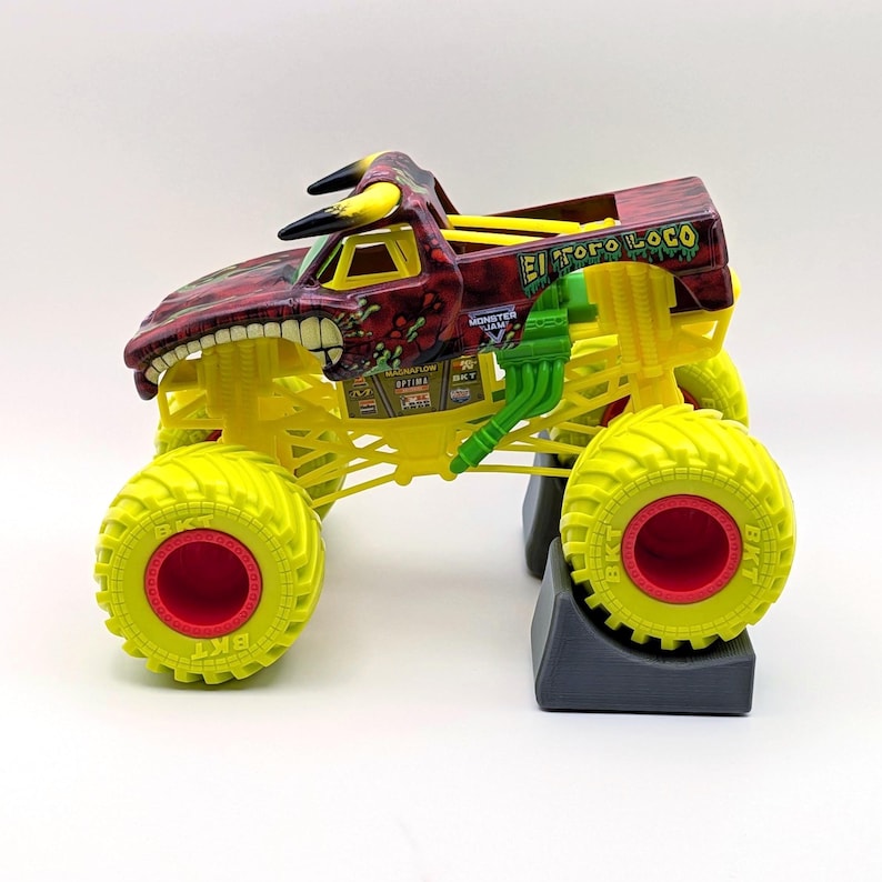 May include: A yellow and red toy monster truck with large wheels. The truck has a red and maroon cab with a bull-like design and the text "El Toro Loco". The wheels are yellow with red centers.