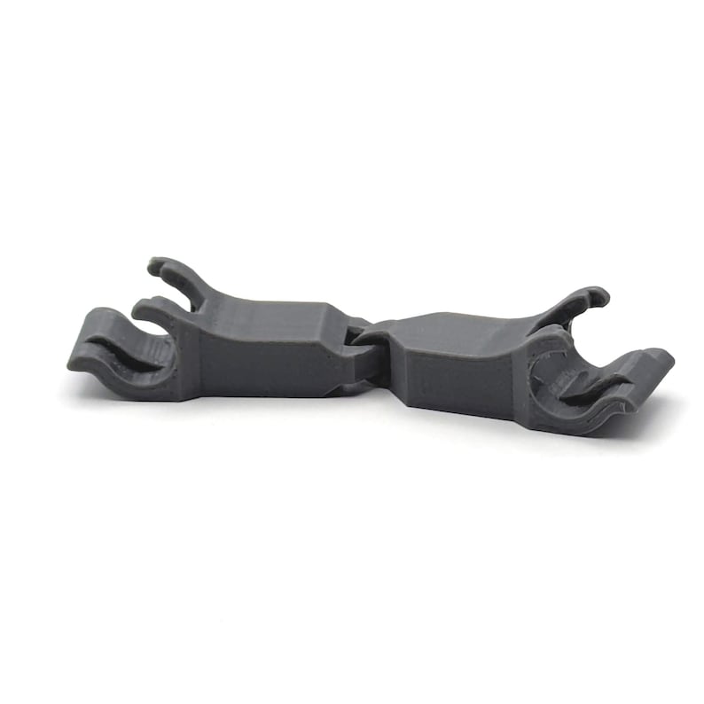 May include: A gray plastic clip with two prongs on each end. The clip is designed to hold two objects together.