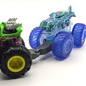 May include: Two toy monster trucks, one green and one blue, with large wheels. The green truck has a skull design and the text "Skeletal Wheels". The blue truck has a shark design and is translucent.