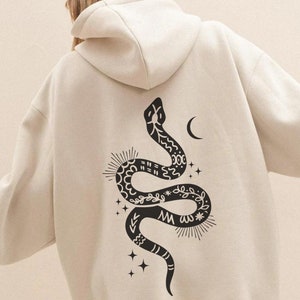 May include: A cream-coloured hoodie with a black and white graphic of a snake with a crescent moon and stars on the back.