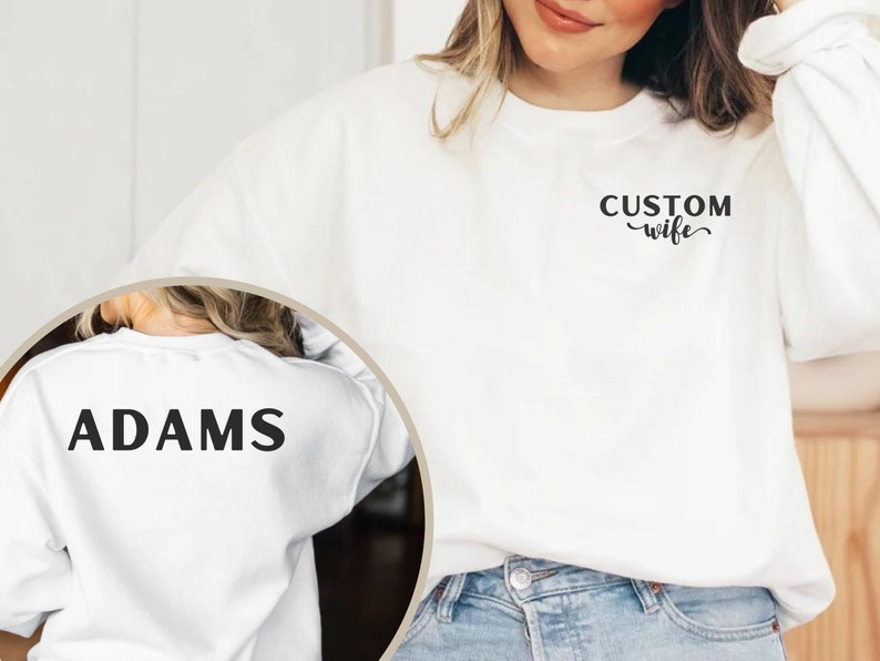 May include: White sweatshirt with the text "CUSTOM wife" on the front and "ADAMS" on the back.