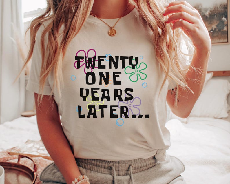 Model wearing white 21st birthday shirt with ‘21 years later’ text and colorful cartoon-inspired flowers and bubbles