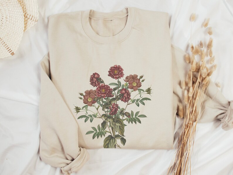 May include: A beige sweatshirt with a floral print featuring a bouquet of pink and red flowers with green leaves.