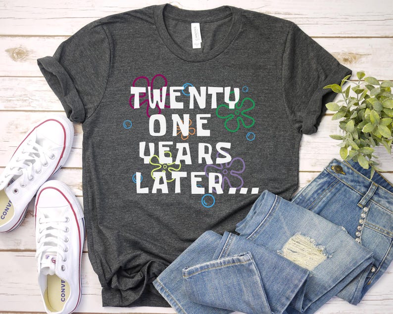 Dark heather 21st birthday shirt flatlay with bold ‘21 years later’ design and fun retro cartoon floral bubble graphics