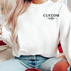 May include: White long-sleeve sweatshirt with the text "CUSTOM wife" printed on the front.