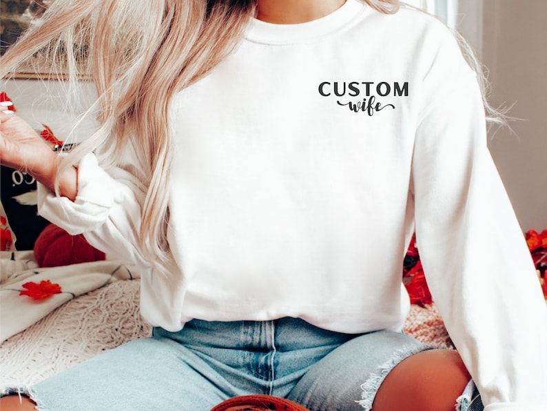 May include: White long-sleeve sweatshirt with the text "CUSTOM wife" printed on the front.