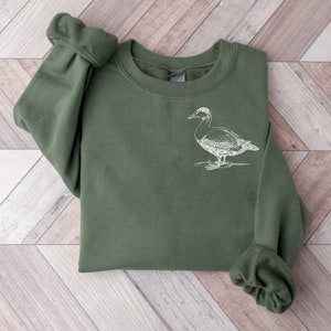 May include: A dark green sweatshirt with a white outline drawing of a duck on the front.