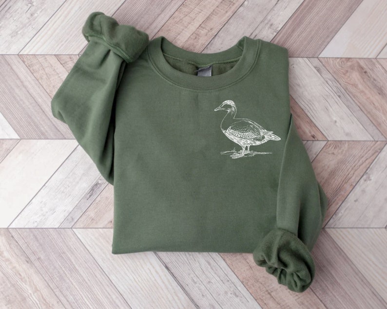 May include: A dark green sweatshirt with a white outline drawing of a duck on the front.