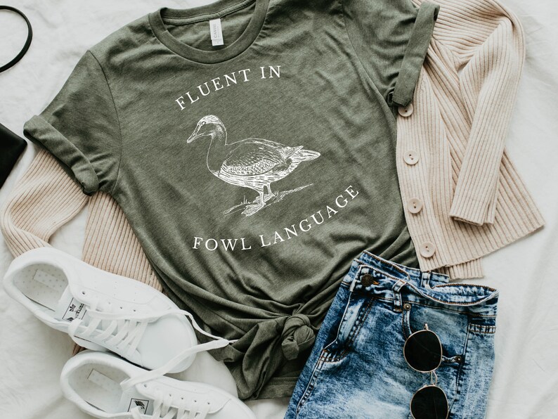 Puede incluir: Una camiseta verde con una ilustraci&oacute;n de pato blanco y el texto "Fluent in Fowl Language".