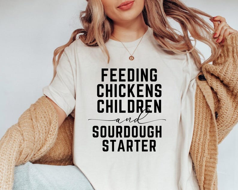 May include: White t-shirt with black text that reads "Feeding Chickens Children and Sourdough Starter".