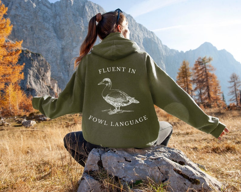 May include: A green hooded sweatshirt with a white graphic of a duck and the text "Fluent in Fowl Language".