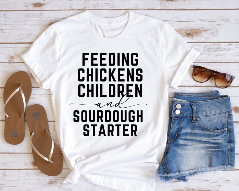 May include: White t-shirt with black text that reads "Feeding Chickens Children and Sourdough Starter".