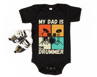 Puede incluir: Mono negro para bebé con un gráfico de estilo retro que dice "Mi papá es el baterista" con una ilustración de batería.