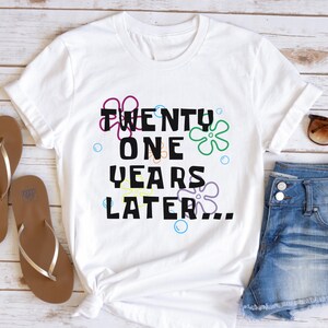 White 21st birthday t shirt flatlay with ‘21 years later’ text and colorful cartoon-style flowers and bubbles design