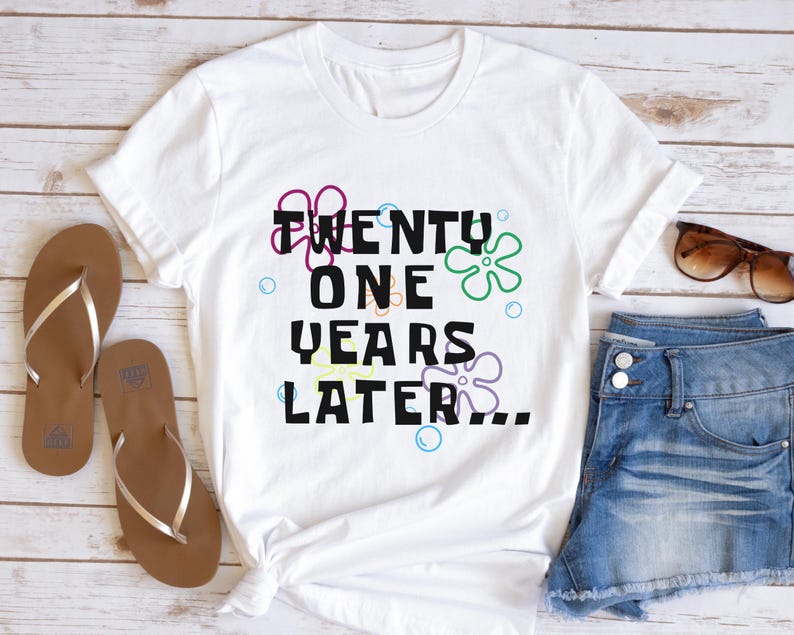 White 21st birthday t shirt flatlay with ‘21 years later’ text and colorful cartoon-style flowers and bubbles design