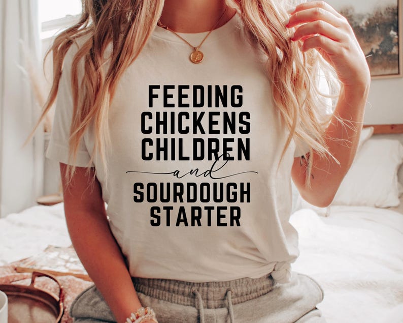 May include: White t-shirt with black text that reads "Feeding Chickens Children and Sourdough Starter".
