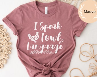 May include: Mauve t-shirt with a white graphic of a chicken and the text "I Speak Fowl Language".