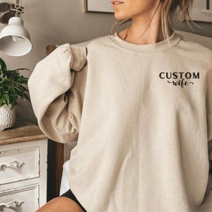 May include: A light beige sweatshirt with the text "CUSTOM wife" printed on the front.