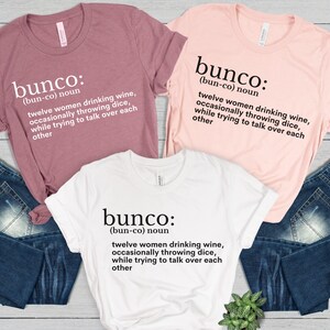 Puede incluir: Tres camisetas con la definici&oacute;n de la palabra "bunco" impresa en ellas. La definici&oacute;n es "(bun-co) sustantivo doce mujeres bebiendo vino, lanzando dados ocasionalmente, mientras intentan hablar por encima de las dem&aacute;s."