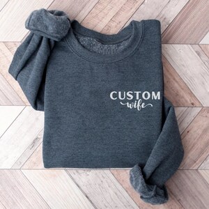 May include: A dark gray sweatshirt with the text "CUSTOM wife" in white lettering.