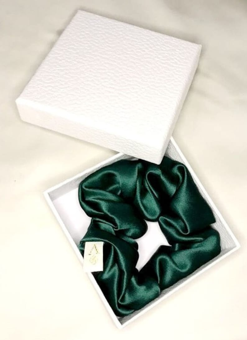 May include: A dark green satin scrunchie in a white box. The scrunchie is made of soft, silky fabric and is perfect for adding a touch of elegance to any hairstyle.