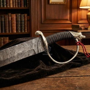May include: A detailed image of a saber with a patterned blade and a black and red wrapped handle. The hilt features a decorative eagle head. The saber rests on a dark cloth, with a wooden background.