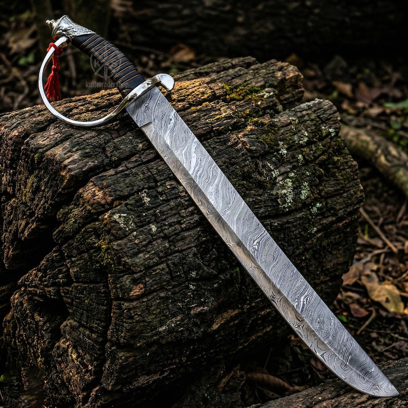 May include: A Damascus steel sword with a silver guard and a black and brown handle. The blade has a unique wave pattern. A red tassel hangs from the guard. The sword is displayed on a weathered wooden surface.