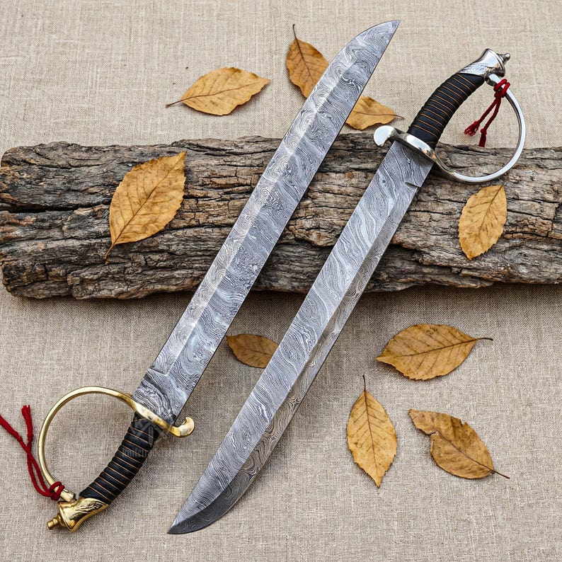 May include: Two Damascus steel swords with curved blades and ornate handles. One sword has a gold-colored hilt and a red tassel, while the other has a silver hilt and a red tassel. The swords are displayed on a piece of wood with autumn leaves.