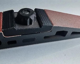 May include: A black sanding block with a red sanding belt attached. The block has a knob for adjusting the tension of the belt.