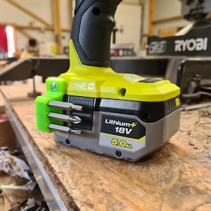 May include: A green and black drill with a yellow battery pack that says "Lithium+ 18V 5.0Ah" and "ONE+". The drill has a green bit holder with three bits attached.