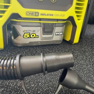 May include: A yellow and black cordless inflator/deflator with a black hose and two nozzle attachments. The device has a digital display and a battery with the text "Lithium+ 18V 5.0Ah" and the brand name "RYOBI".