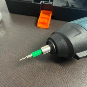 May include: A close-up of a black and green electric screwdriver with a green bit attached.