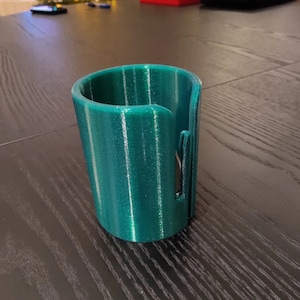 May include: A teal green 3D printed phone stand with a slot for charging cables.