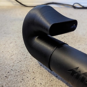 May include: A black plastic leaf blower nozzle with a curved extension. The nozzle has a rectangular opening at the end.