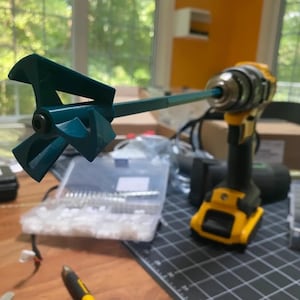 May include: A teal blue paint mixer attachment for a drill. The mixer has four blades and is attached to a long, silver shaft. The drill is yellow and black.