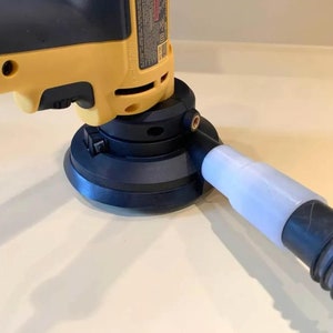 May include: A yellow and black power sander with a dust collection hose attached. The sander is on a white surface.