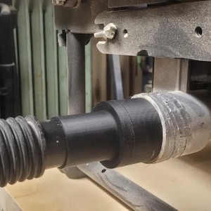 May include: A black dust collection hose connected to a grey dust port on a woodworking machine.