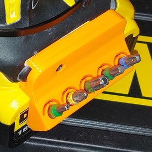 May include: Orange plastic holder with six slots for holding screwdriver bits. The holder is attached to a yellow and black power drill. The screwdriver bits are different colors and sizes.