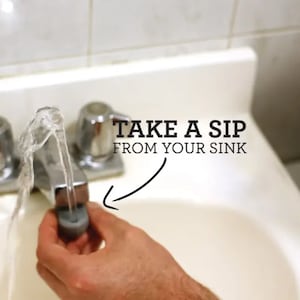 May include: A close-up of a bathroom sink with a faucet running. The water is flowing into a gray plastic cup. The text "TAKE A SIP FROM YOUR SINK" is written above the sink.