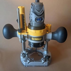 Puede incluir: Una fresadora DeWalt amarilla y negra con una fresa gris. La fresadora tiene un indicador de profundidad y una base transparente.