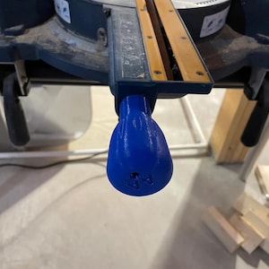 May include: A blue plastic lever with a textured surface and a small arrow pointing to the right. The lever is attached to a piece of machinery.