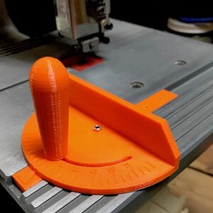 May include: Orange plastic jig with a handle and a protractor for a table saw. The protractor has markings in degrees.